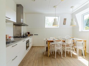 A modern kitchen with white cabinetry, a wooden dining table, and white chairs. - Luxurious Apartment in Koudekerke with Parking (Koudekerke)