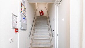 Eine schmale Treppe mit einem Feuerlöscher an der Wand, einem Feueralarm und einer Tür am Fuß.