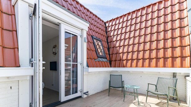 Eine überdachte Terrasse mit Holzboden, einer Glastür zum Innenbereich und zwei Metallstühlen.