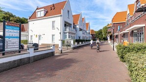 Eine straßenpflasterte Gasse gesäumt von traditionellen Gebäuden mit weißen und roten Dächern, ein Schild mit Schrift und zwei Radfahrer.