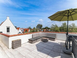 Une terrasse sur le toit aménagée avec un canapé d’angle, un jardinier en bois et une table avec des chaises.