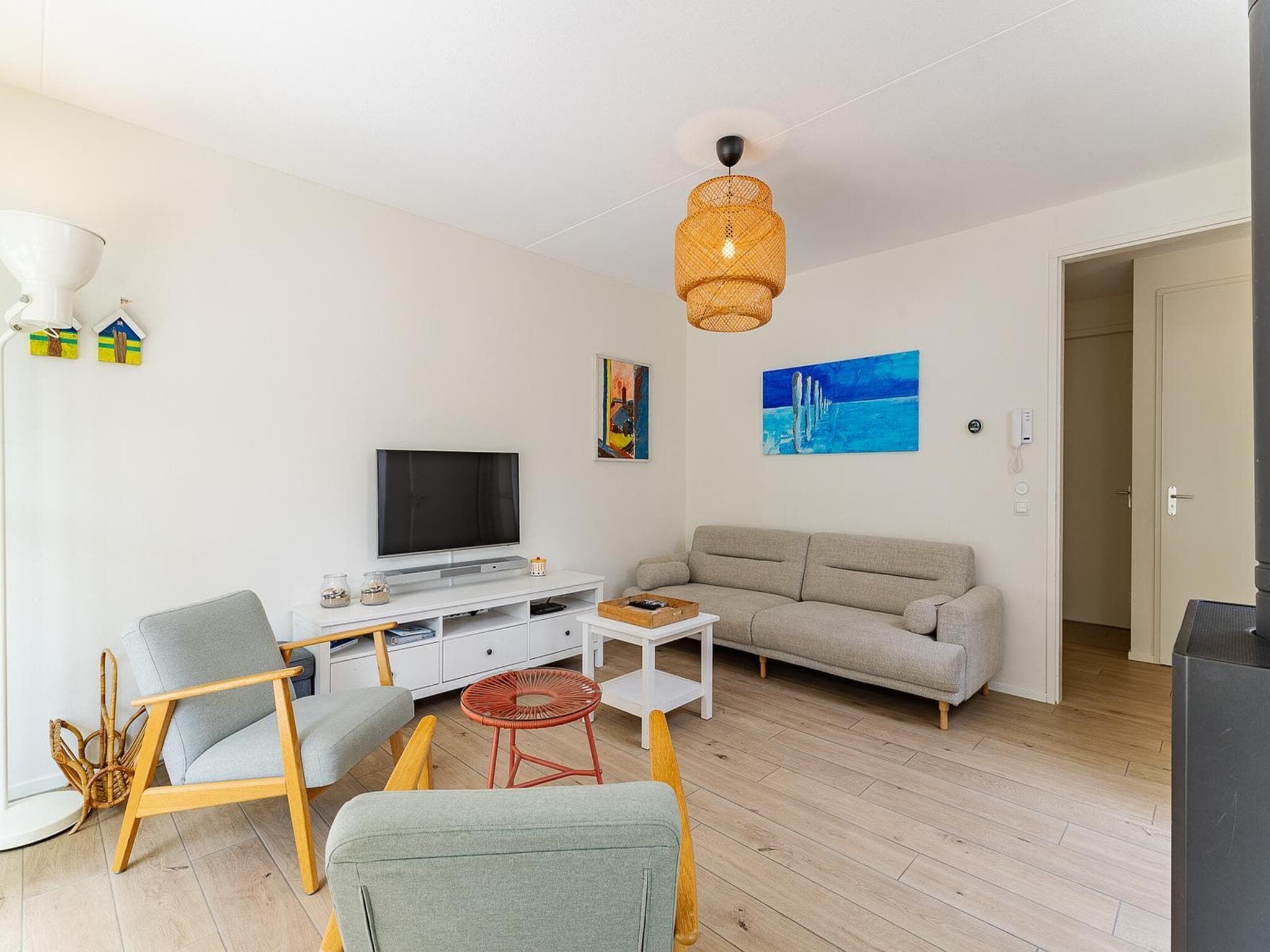 Una sala de estar moderna con televisor de pantalla plana, un sofá, una mesa de centro y una silla de mimbre.