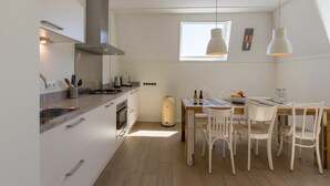 Eine moderne Küche mit weißen Schränken, einem Gasherd und einem Essbereich mit weißen Stühlen und einem Holztisch.