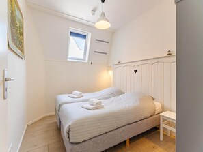 A bedroom with two beds, a window, a white ceiling, and a white wall.