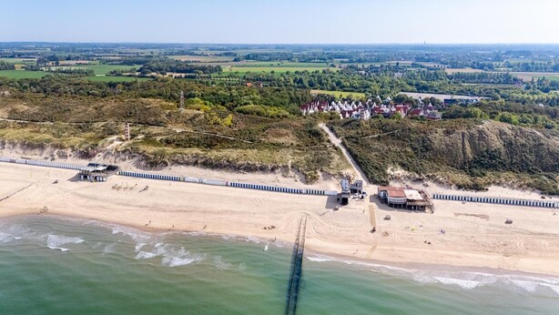 Eine Luftaufnahme einer Küstenlandschaft mit Strand, Bahnlinie und einer Häuserreihe.