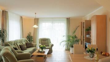 En stue med sofa, lænestol, sofabord og et træskab med plante og skålsætning frugt.