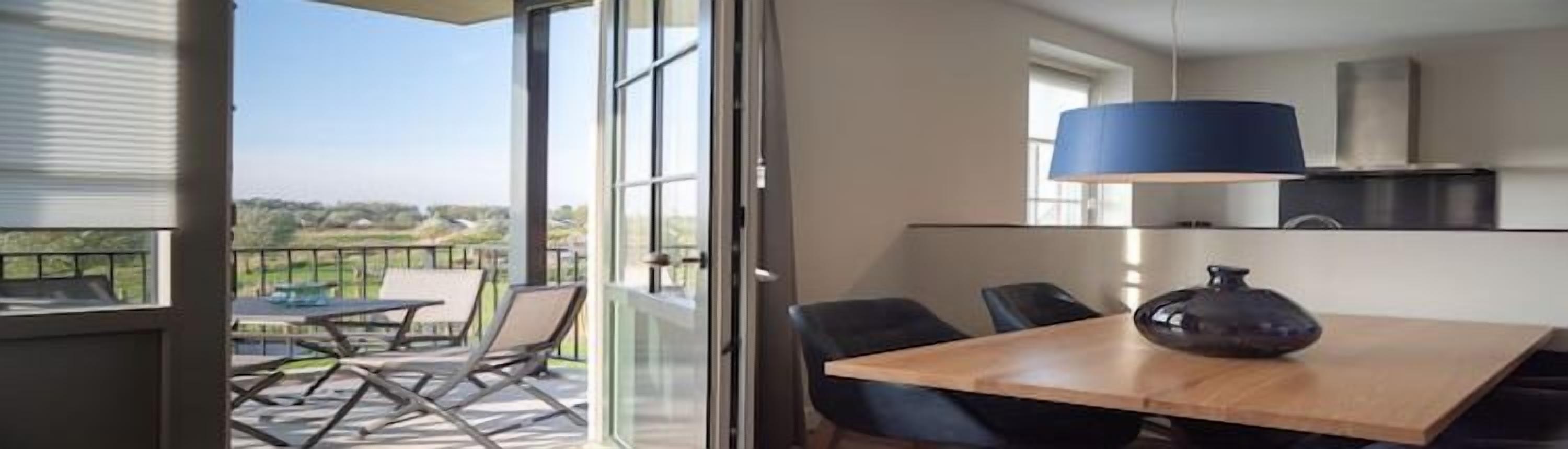 Una cucina moderna con un'ampia lampada a sospensione blu, un tavolo da pranzo con sedie e vista sull'esterno attraverso una porta scorrevole in vetro.