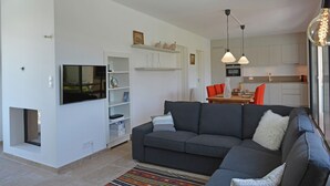 Ein modernes Wohnzimmer mit grauem Sofa, einem Flachbildfernseher und einer Küche im Hintergrund.