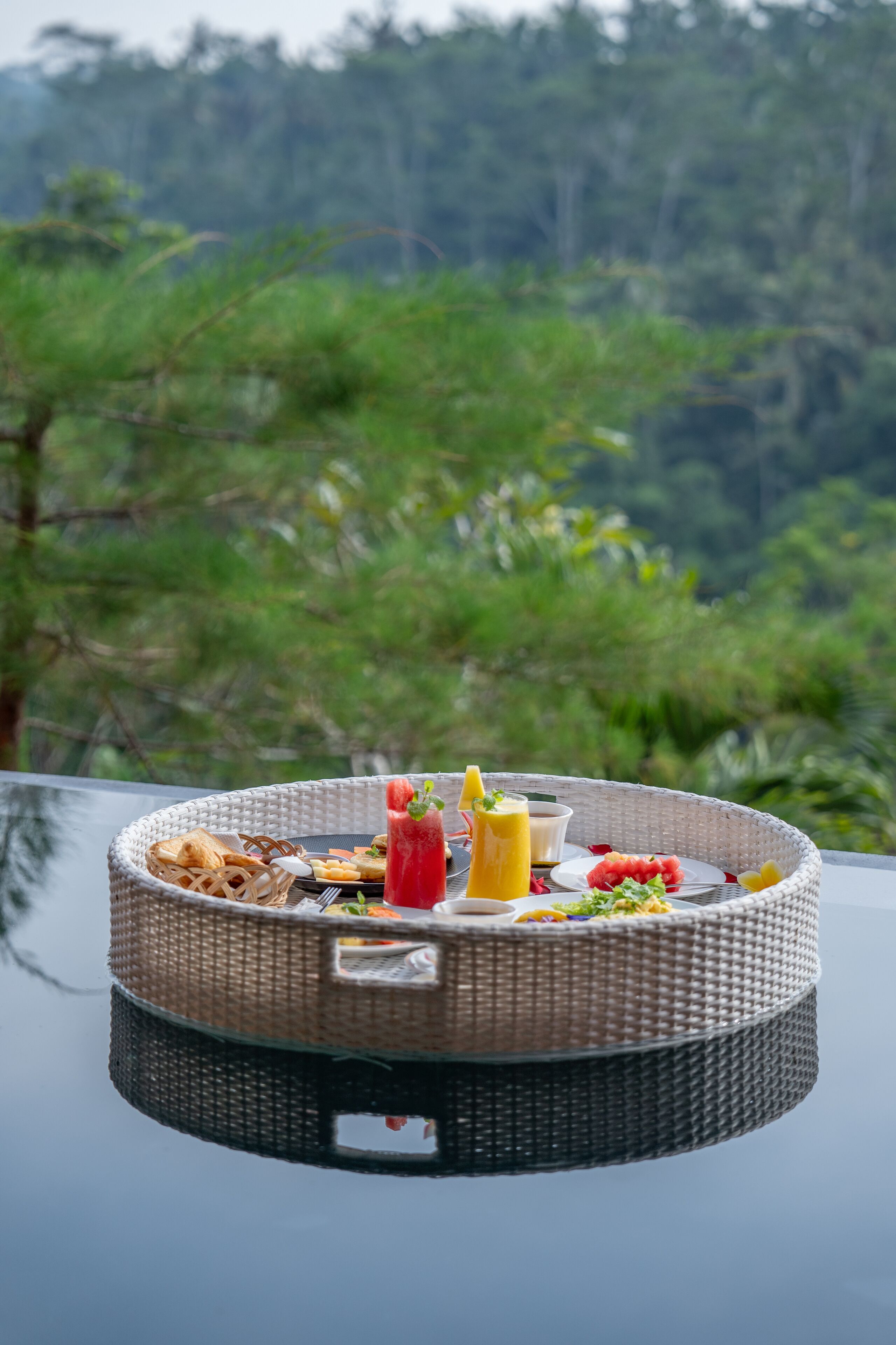 A wicker tray with food and drinks on a table with a forest view.
