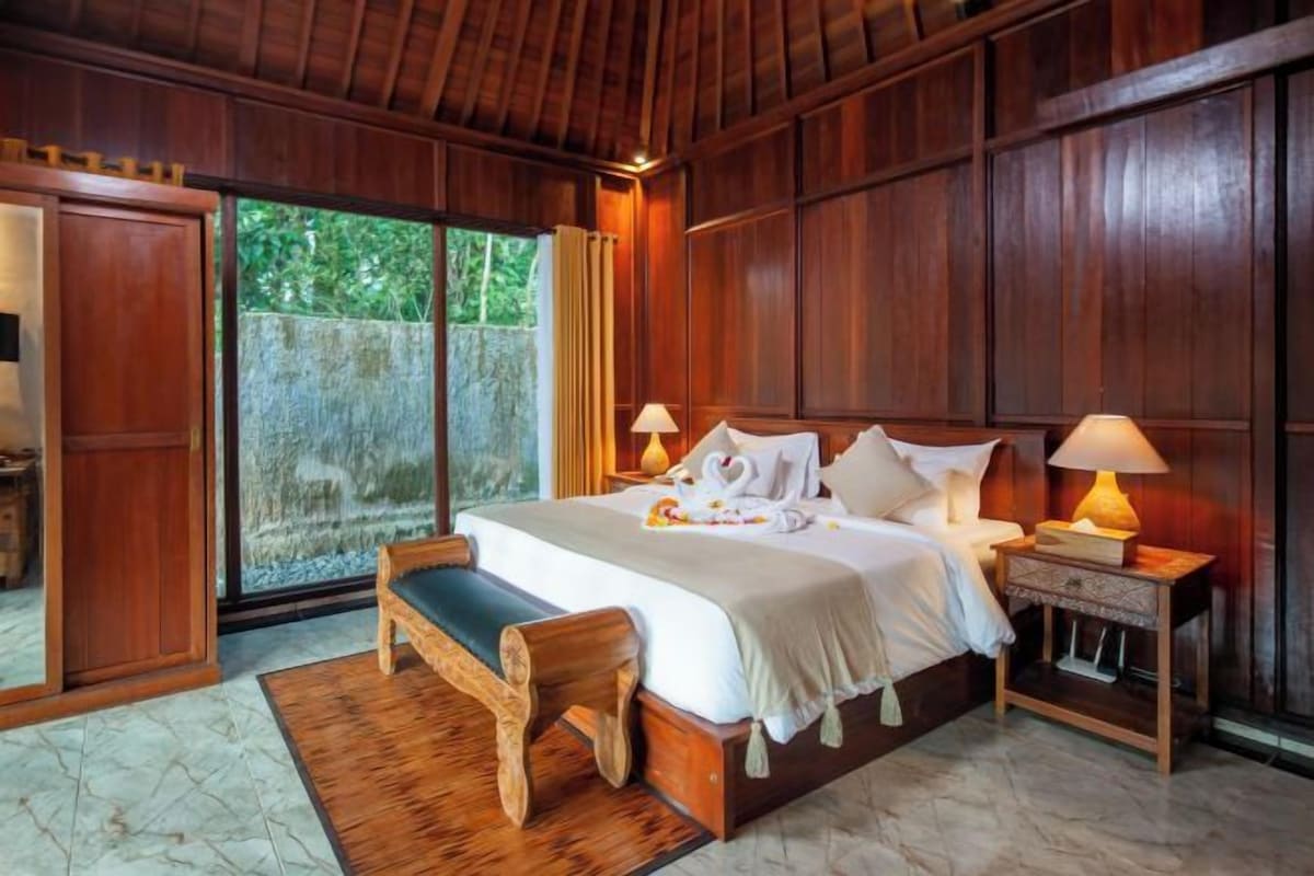 A spacious bedroom with a large bed, wooden headboard, bedside lamps, and a bench.