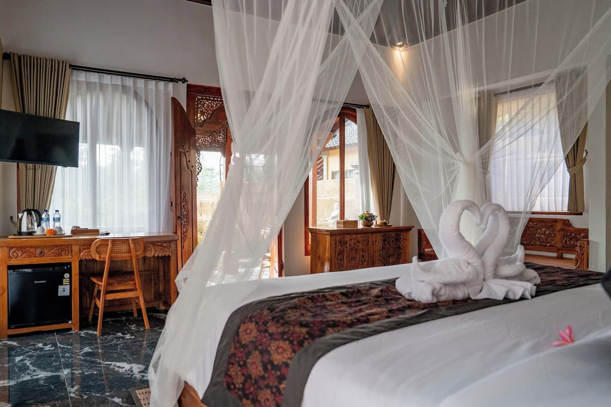 Quarto de hotel com cama, escrivaninha, televisão e suporte para TV.