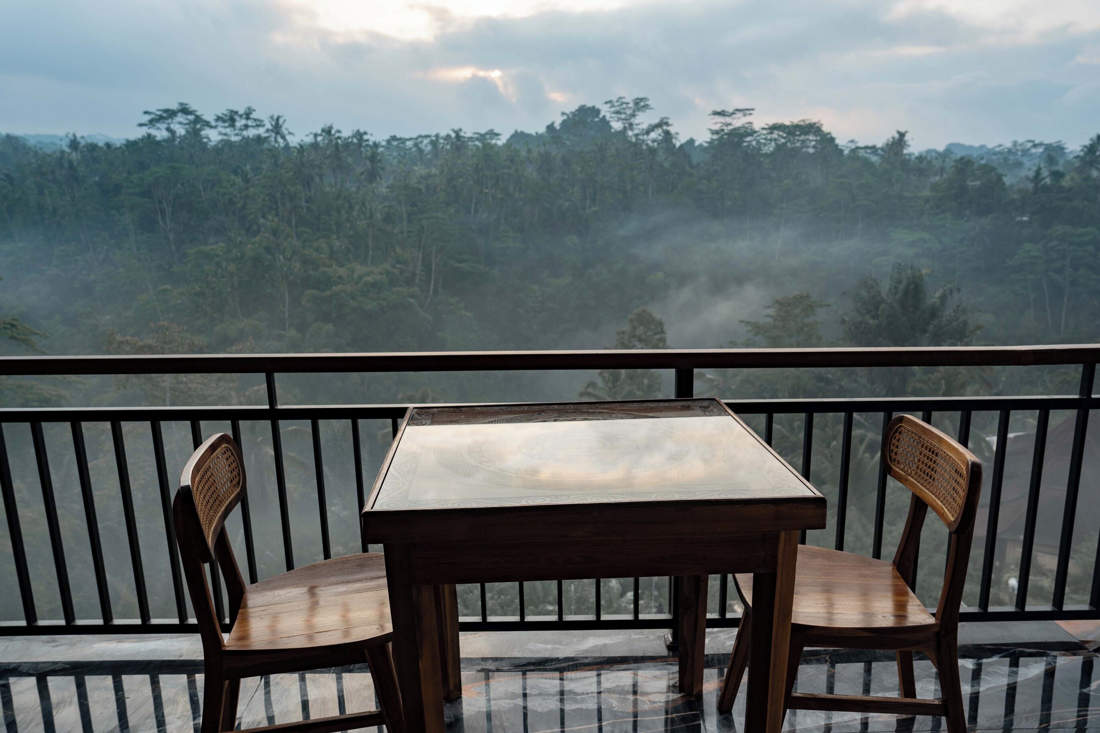 Un balcón con dos sillas de madera y una mesa, con vistas a un paisaje boscoso.