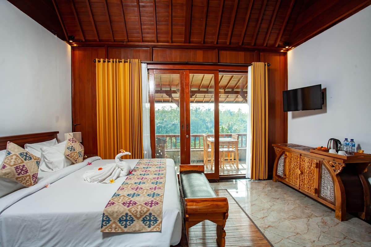 Quarto de hotel com cama, um banco, televisão e varanda com vista.