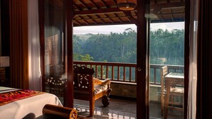 A room with a bed, a wooden bench, and a balcony with a view of a forested area. - Campuhan Sebatu Resort (Sebatu)