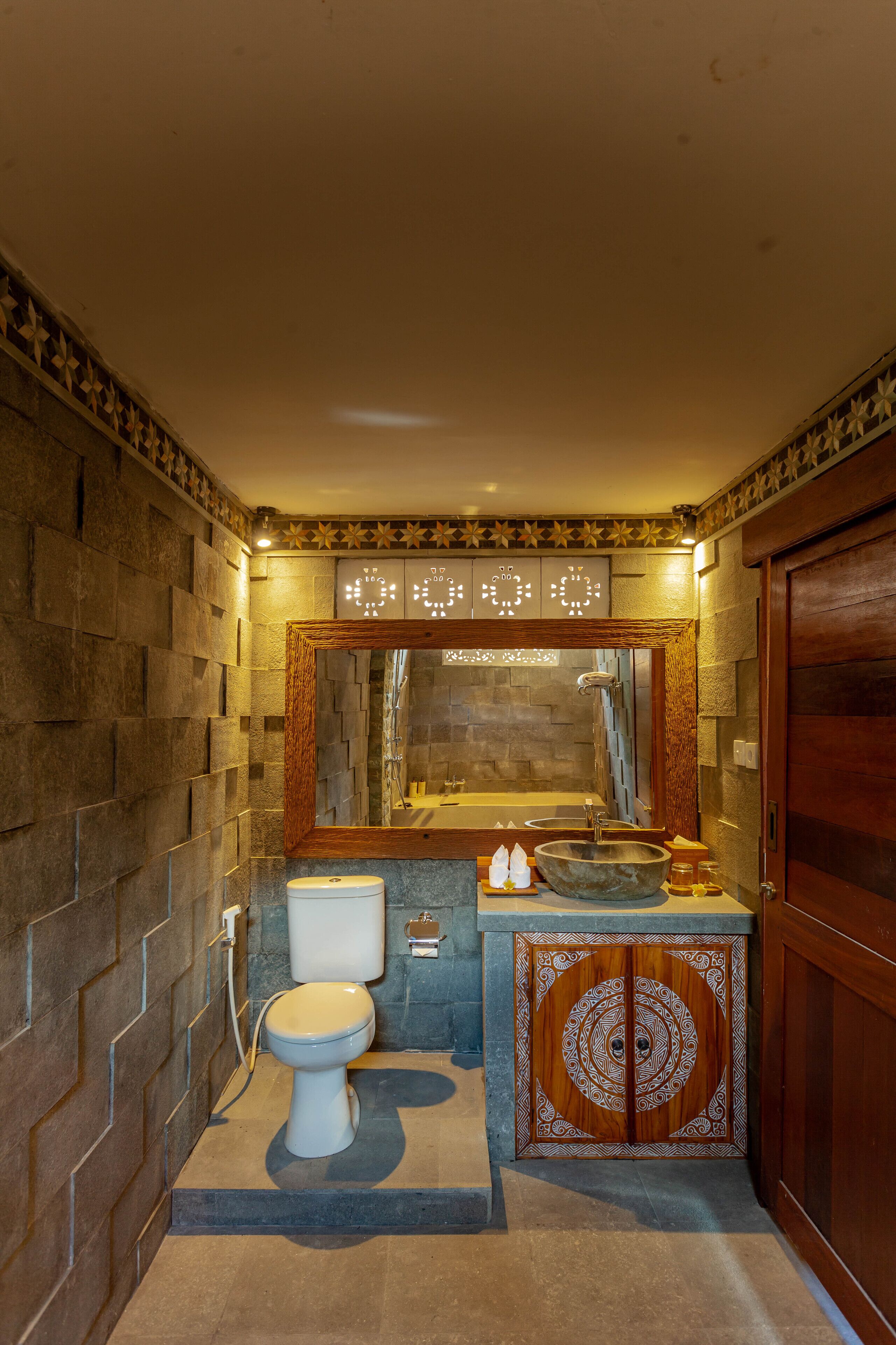 Un baño con pared de piedra, tocador de madera, un espejo grande y una puerta de madera.