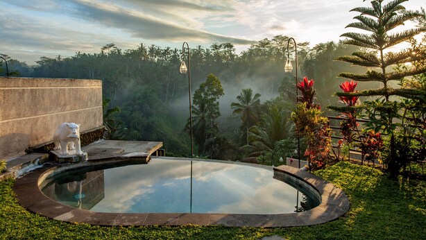 A serene outdoor pool area with a stone statue, surrounded by lush greenery and palm trees. - Campuhan Sebatu Resort (Sebatu)