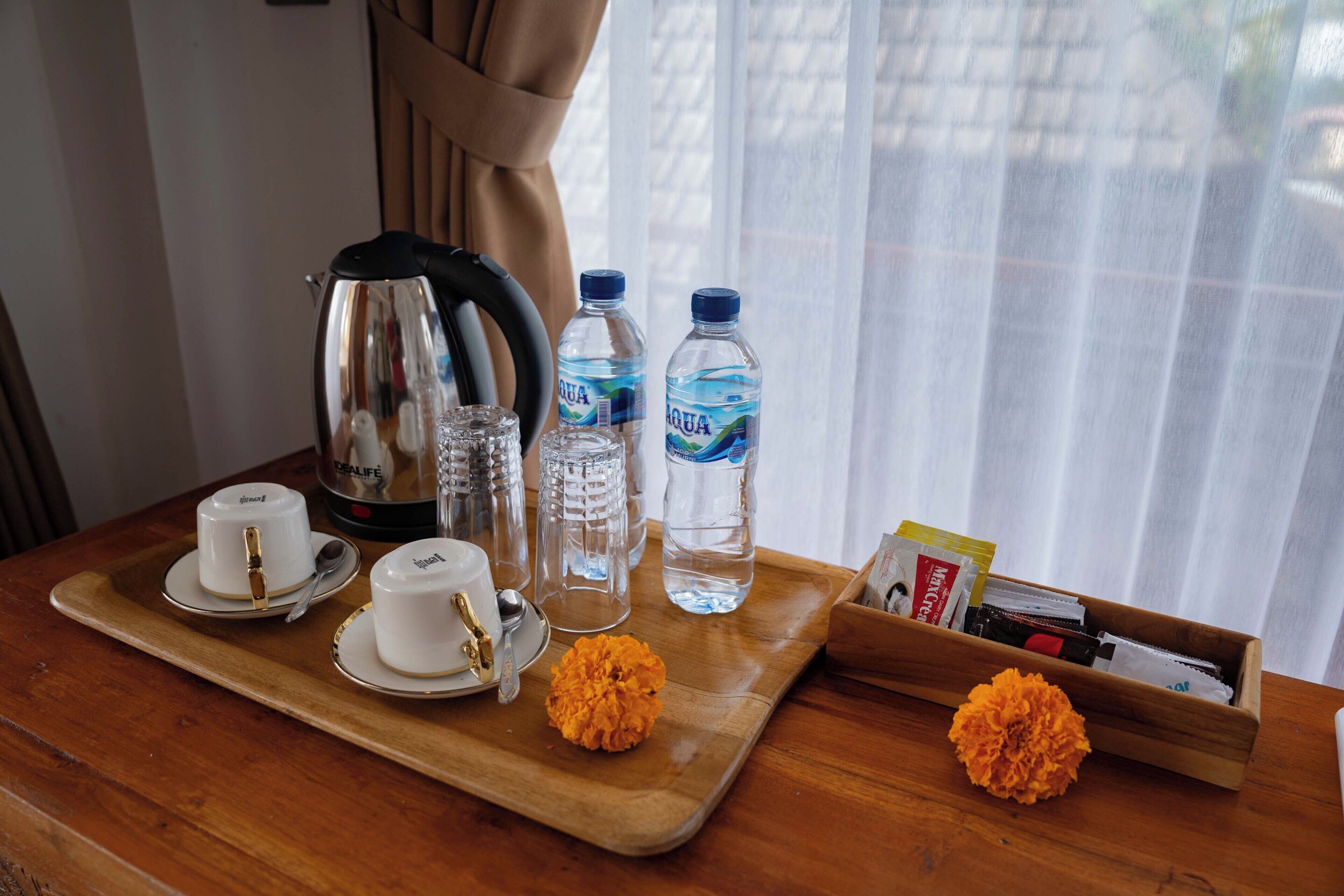 A wooden tray with cups, a kettle, water bottles, and a small box of tissues.