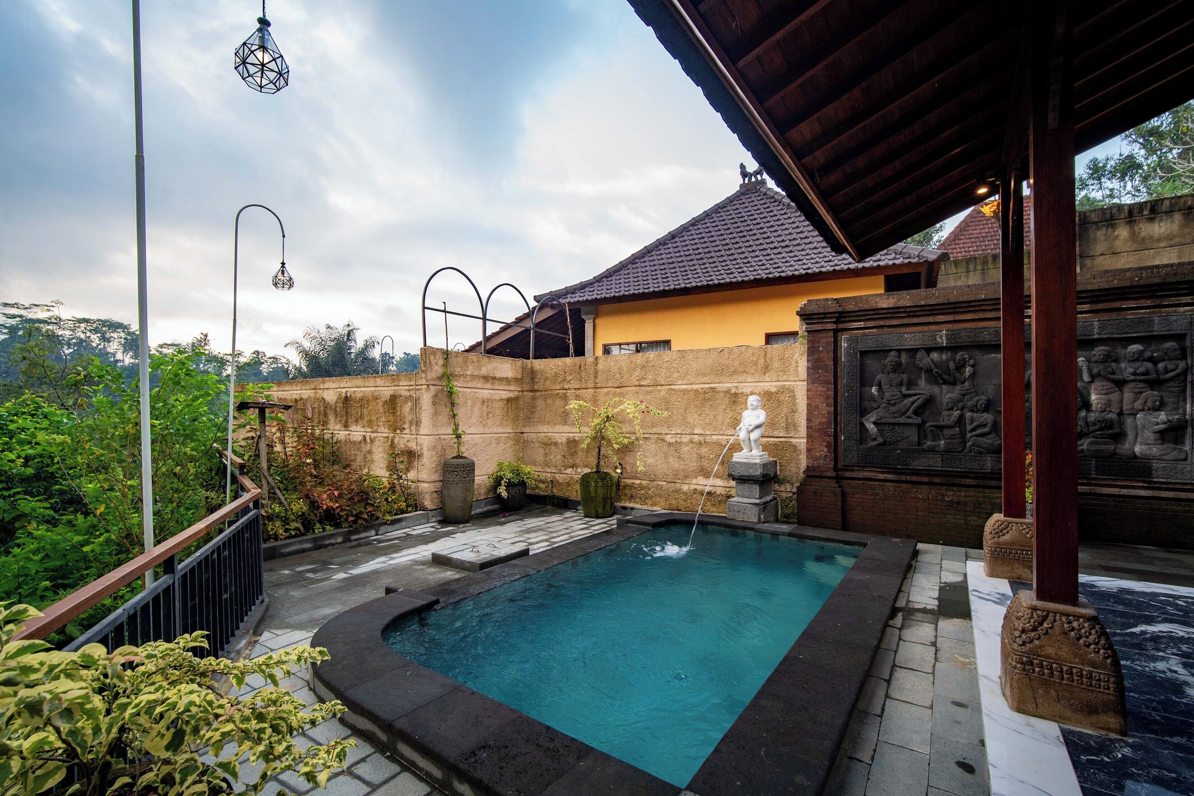 A swimming pool with a stone border, a covered area with a tiled roof, and a statue.