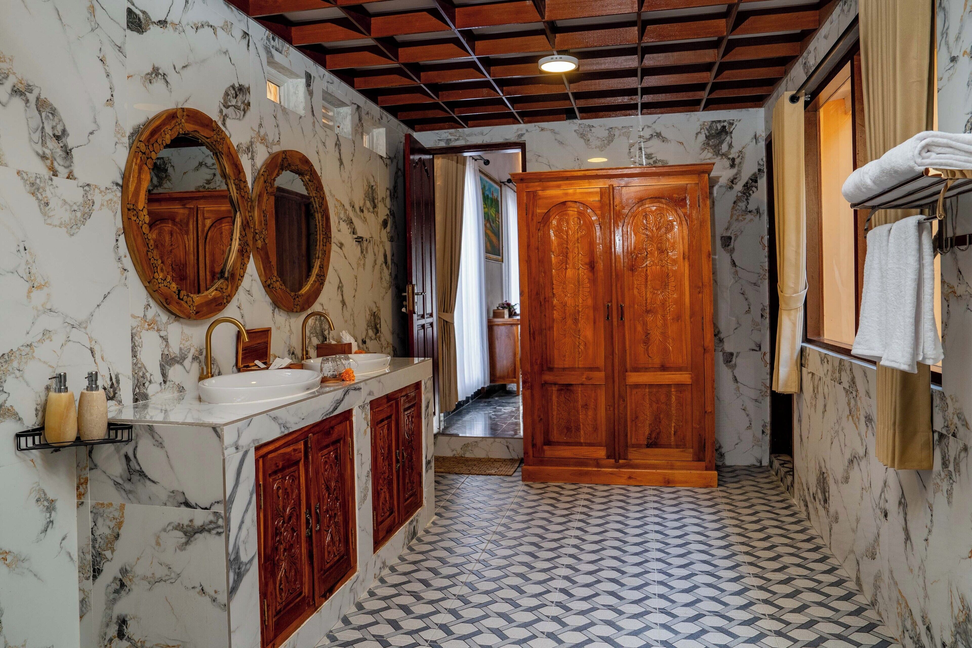Un baño con paredes de mármol, un tocador de madera, dos espejos redondos y un suelo con diseño.