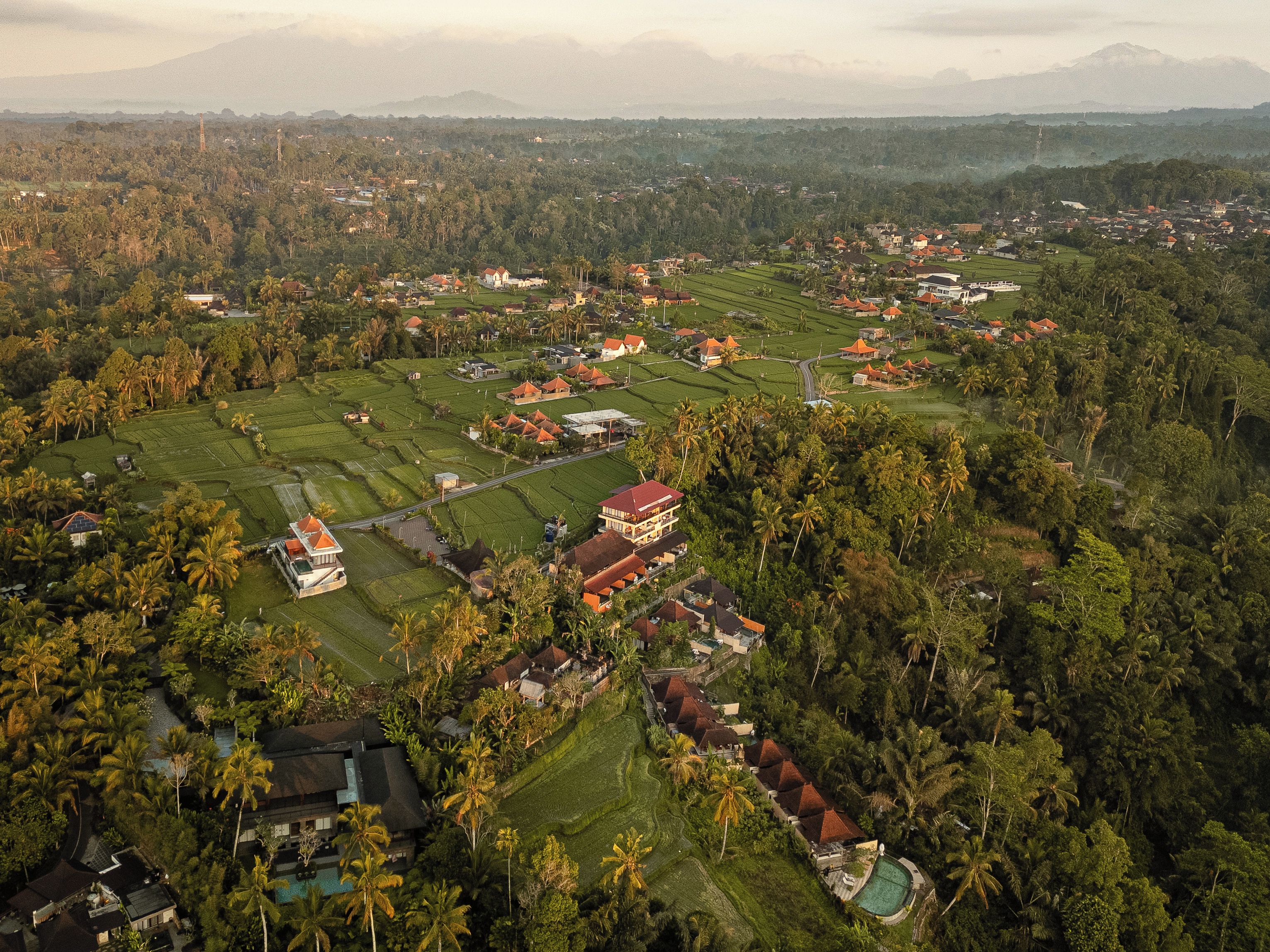 An aerial view of a rural area with scattered houses, green fields, and a mountain in the background.