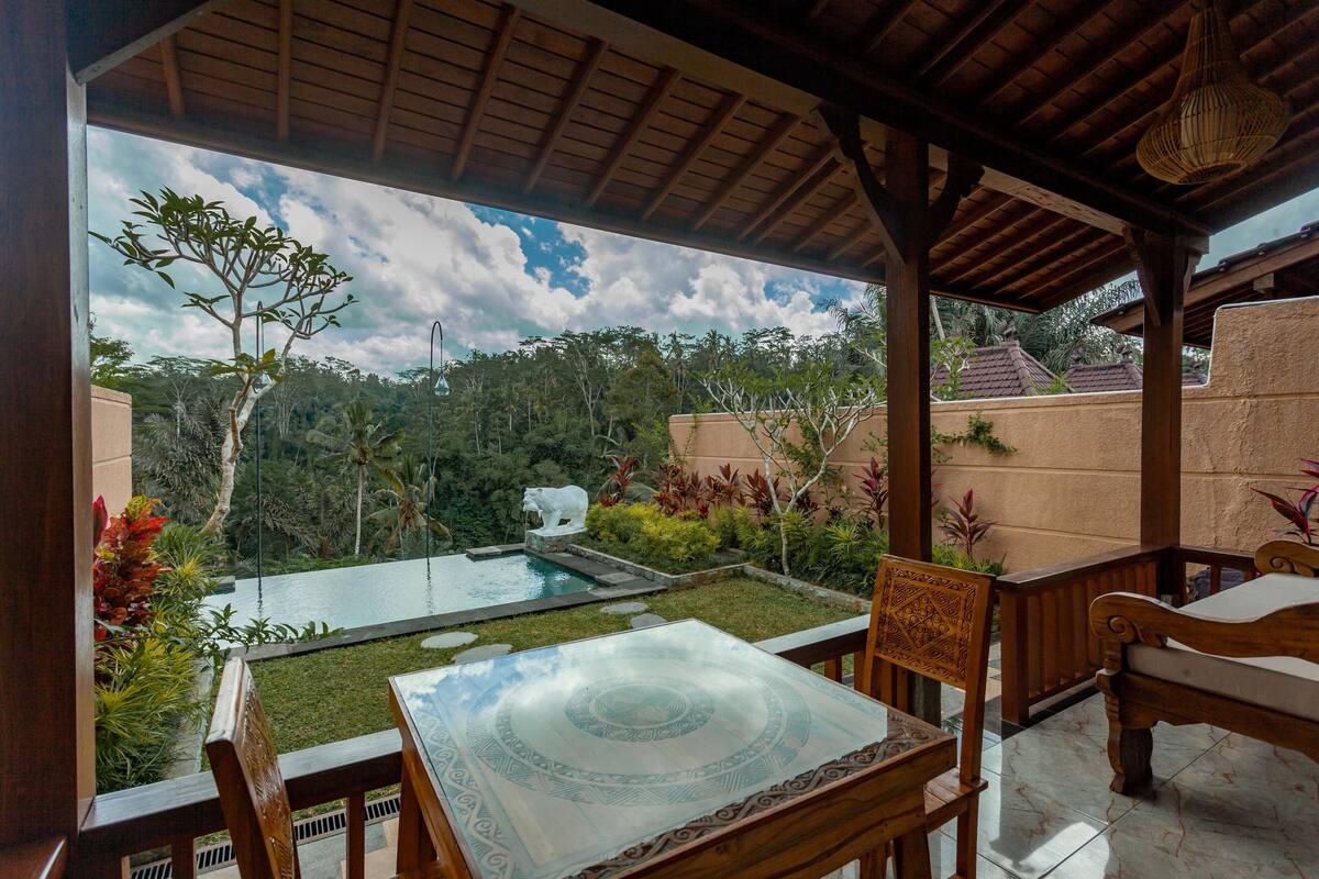 Uma área externa coberta com piscina, móveis de madeira e vista para uma paisagem tropical.