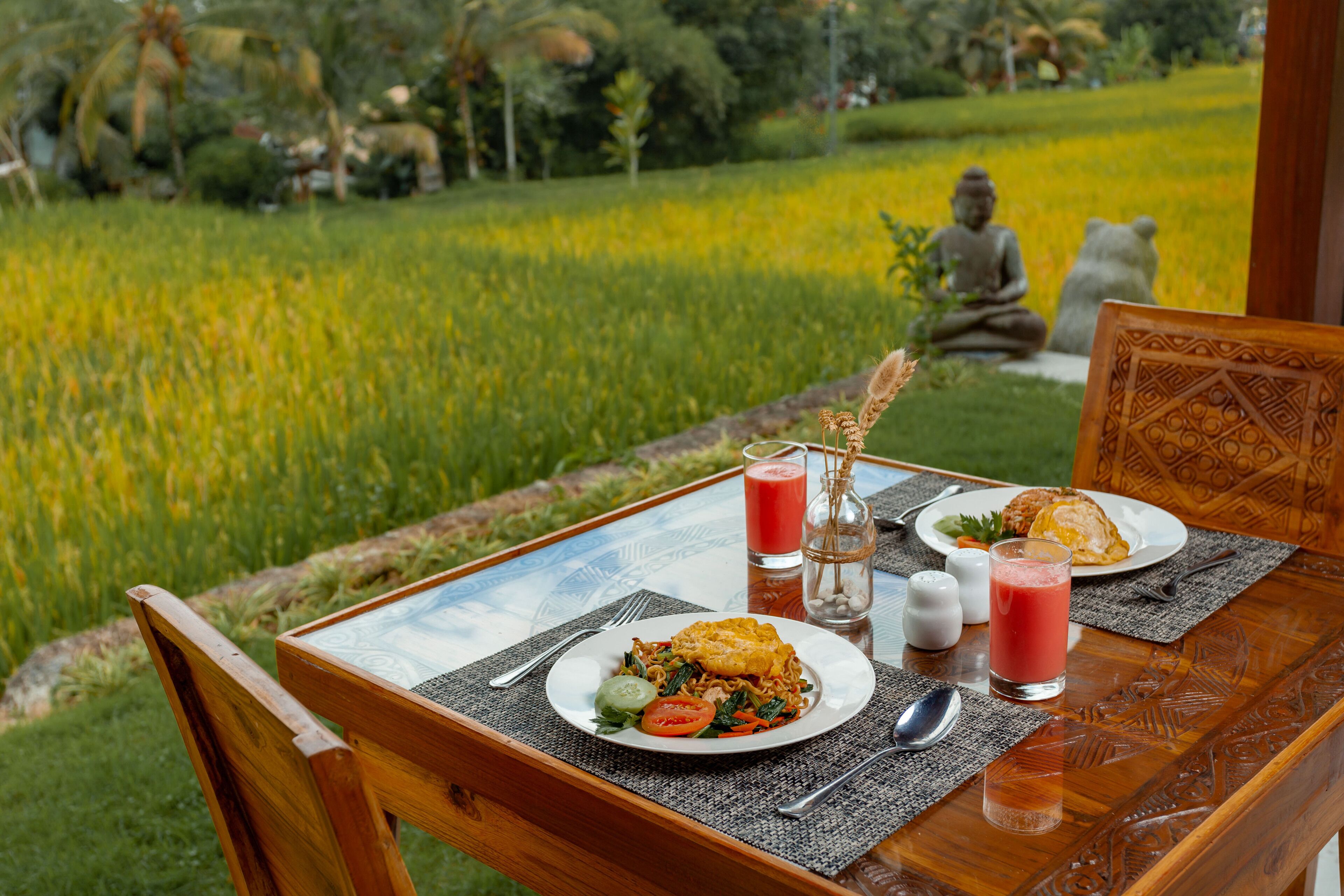 Une table dressée avec un repas, un verre de jus de fruits et une statue de Bouddha en arrière-plan.