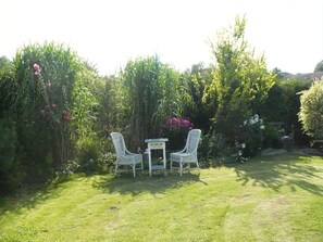 Un giardino con due sedie bianche e un tavolino, immerso nel verde rigoglioso e tra piante fiorite.