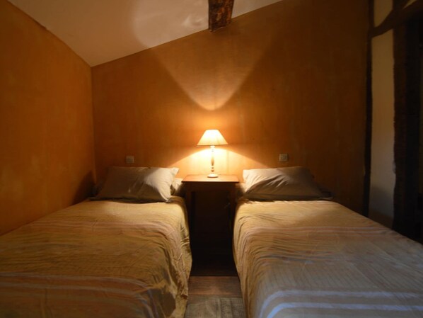 A small, dimly lit room with two single beds, a nightstand with a lamp, and wooden walls. - Holiday Home in Thurageau with Private Pool (Lencloître)
