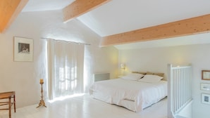 Un dormitorio con una cama grande, una silla de madera, una mesita de noche y una ventana con cortinas.