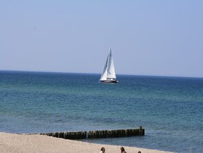 Un velero en aguas tranquilas, con una playa de arena en primer plano.