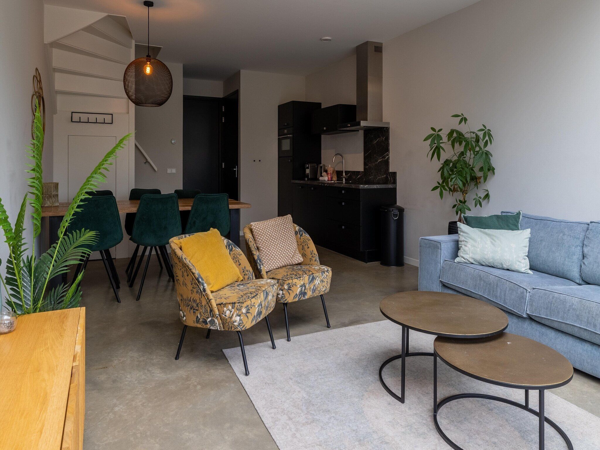 Ein modernes Wohnzimmer mit einer Couch, zwei Sesseln, einem Couchtisch und einem Essbereich mit Stühlen und Tisch.