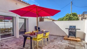 Un patio al aire libre con una mesa, sillas, un paraguas rojo y una parrilla.
