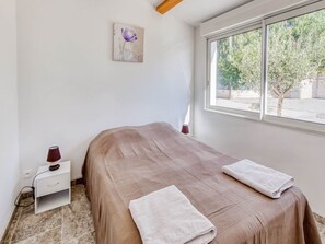 Un dormitorio con cama, mesita de noche, lámpara y ventana con vistas a árboles.