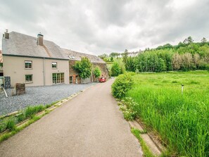A rural property with a gravel driveway leading to a house with stone and brick walls, a red car parked outside, and a lush green field. - Riverside Villa with Charm (Léglise)
