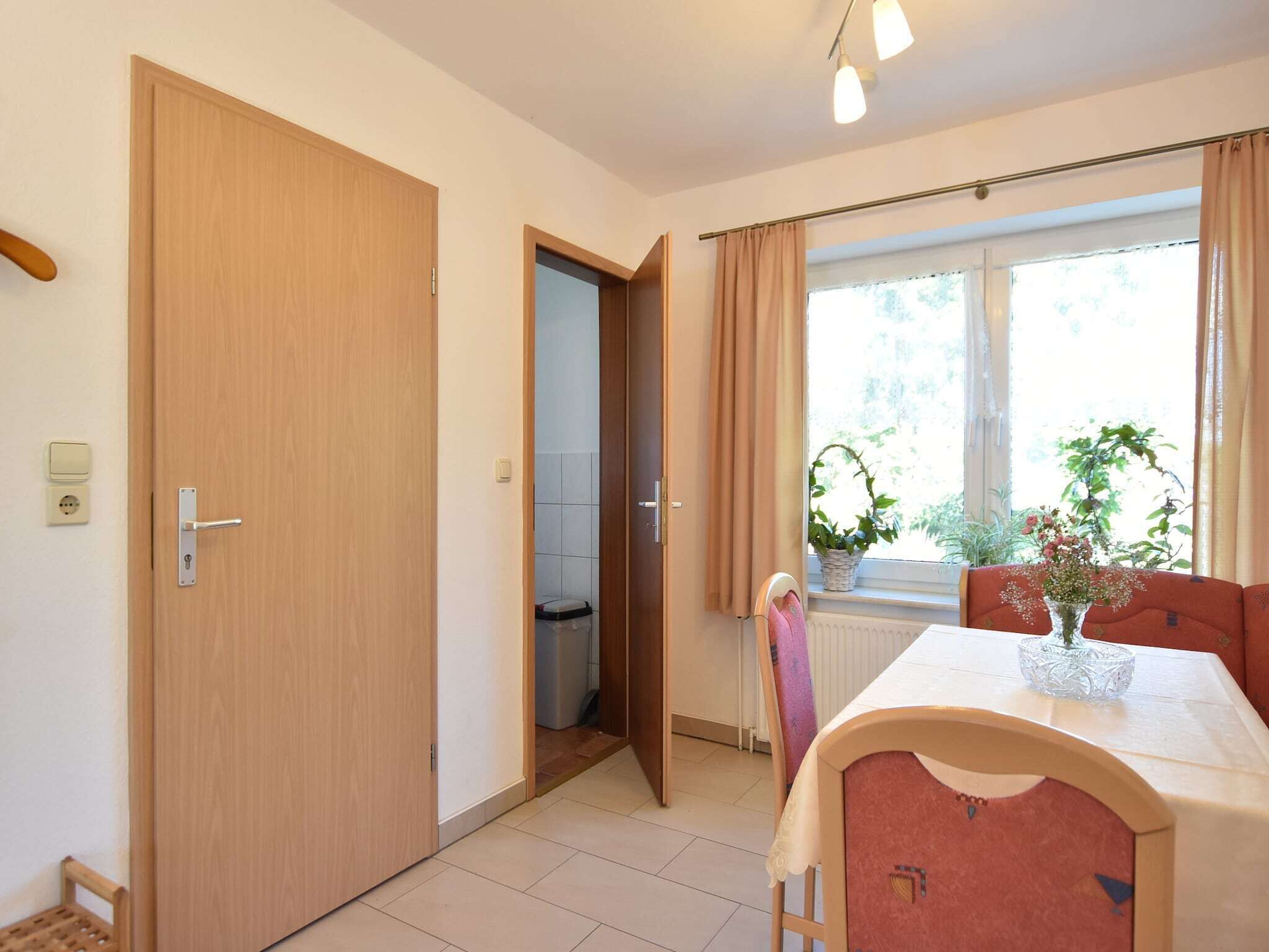 Une pièce avec une porte en bois, une fenêtre avec des rideaux, une table recouverte d’une nappe et une chaise.
