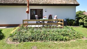 A thatched-roof house with a wooden bench in front, a table with chairs, and a garden with various plants. - Wohnung in Pepelow in Meeresnהhe (Pepelow)