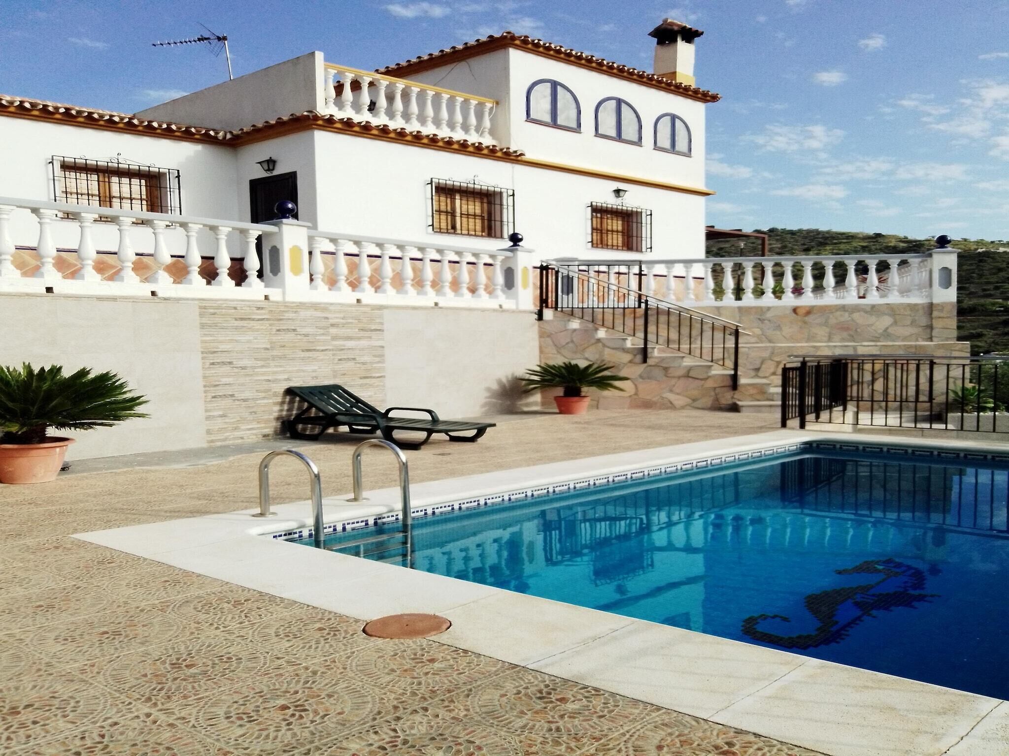 A poolside area with a pool, a white building with balconies, and a stone wall.