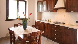 A kitchen with wooden cabinets, a gas stove, and a window with curtains. - Elegant Country Villa in Cagli (Cagli)