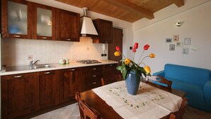 A kitchen with wooden cabinets, a gas stove, and a blue vase with flowers on a table. - Elegant Country Villa in Cagli (Cagli)