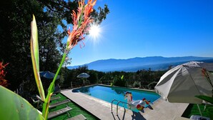 A swimming pool with a view of mountains, surrounded by lounge chairs and umbrellas.