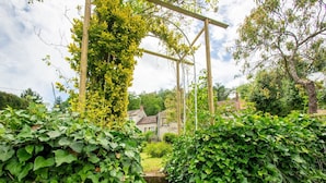 Un camí de jardí amb una pergola de fusta coberta d'ivarn, que condueix a una casa amb teulada tradicional.