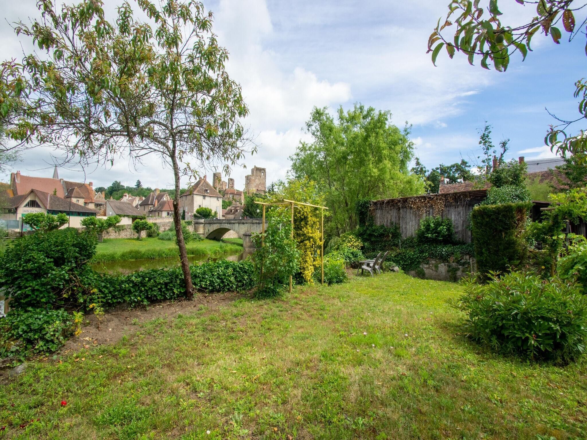 Un patio rural con un puente de piedra, exuberante vegetación y edificios tradicionales al fondo.