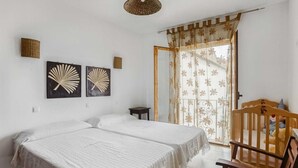 Een slaapkamer met twee bedden, een houten stoel, een klein tafeltje en een raam met een bloemen gordijn.