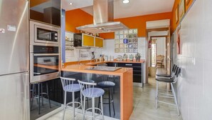 Een moderne keuken met roestvrijstalen apparatuur, een centraal eiland met barkrukken, en uitzicht op de eetruimte.