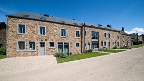 A row of stone buildings with multiple windows and doors, a paved driveway, and a clear blue sky. - Charming Rural Retreat (Bourseigne-Neuve)