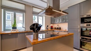 A modern kitchen with a central island, stainless steel appliances, and a view of the outside through large windows. - Charming Rural Retreat (Bourseigne-Neuve)
