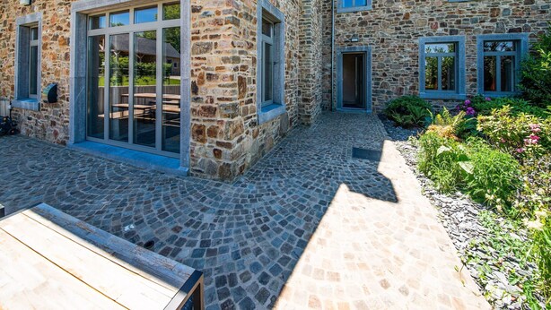 A stone building with large glass doors and windows, a cobblestone patio, and a garden area with plants. - Charming Rural Retreat (Bourseigne-Neuve)