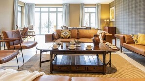 A spacious living room with a brown leather sofa, a wooden coffee table, and a dining area with chairs and a table. - Charming Rural Retreat (Bourseigne-Neuve)