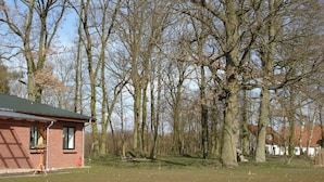 A rustic building with a brick exterior and a green roof, surrounded by a grassy area and tall trees.