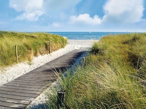 Une promenade en bois qui mène à une plage bordée de dunes de sable, sous un ciel dégagé.
